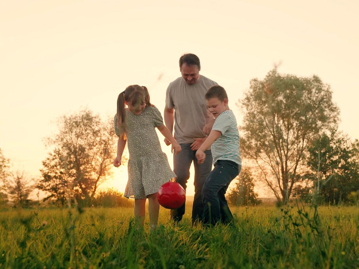 Ein Mann steht mit einem Jungen und einem Mädchen auf einer Wiese und spielt mit einem Ball