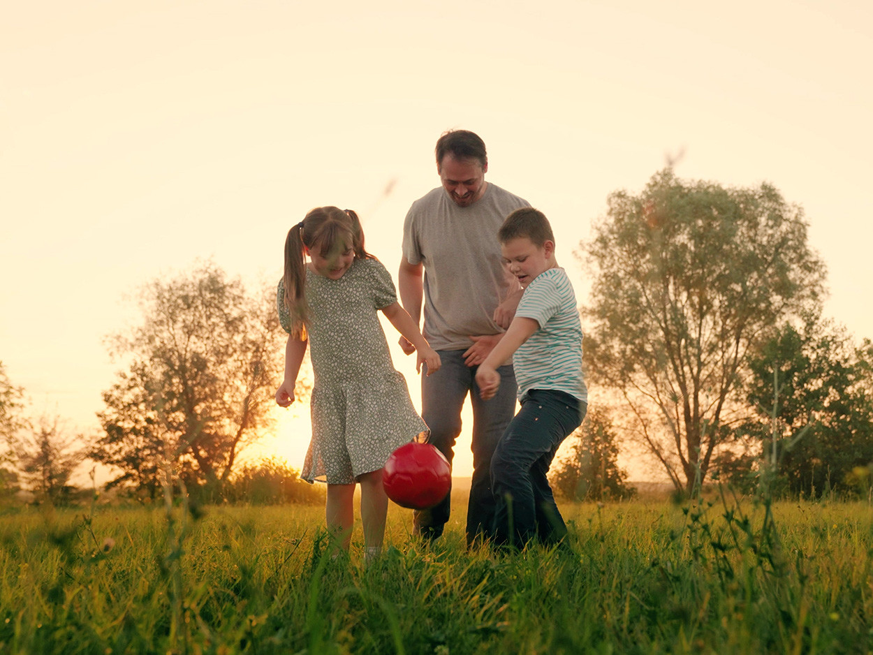 Ein Mann steht mit einem Jungen und einem Mädchen auf einer Wiese und spielt mit einem Ball