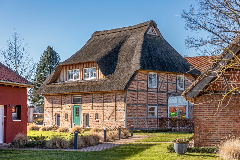 Befestigter Weg auf dem Hofgut Bockelkathen zwischen einem Gebäude mit rotem Putz und Scheunengebäude, der zum Hauptgebäude führt
