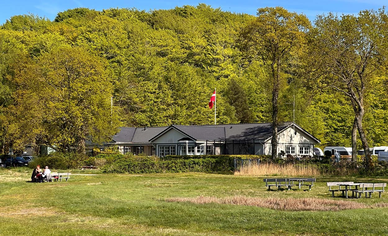 Wiesenfläche mit Picknick-Bänken und dem Rezeptionsgebäude vom Campingplatz Galsklint im Hintergrund.