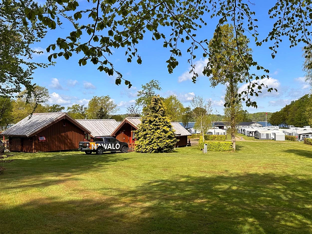 Aufnahme vom Campingplatz Galsklint mit Holzhütten auf der linken Seite und Campingwagen auf der rechten Seite.